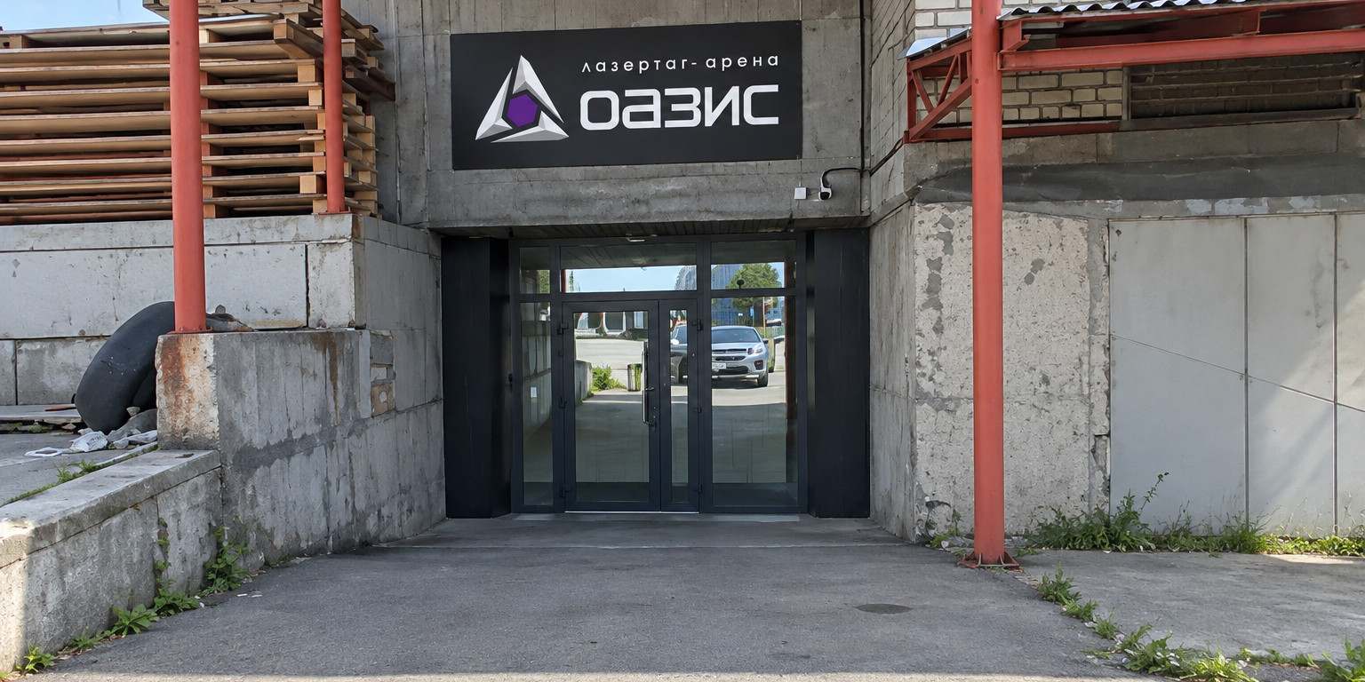 Вход в ОАЗИС: чёрная вывеска с логотипом над стеклянной дверью